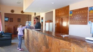 A reception desk with a wooden counter, a calendar, and a sign for Hotel Atlantico. - Hotel Atlantico Costanera (Santa Teresita)