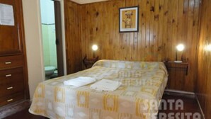 A bedroom with a wooden paneled wall, a bed with a patterned bedspread, two bedside lamps, and a framed picture on the wall. - Hotel Atlantico Costanera (Santa Teresita)