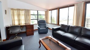 Un vaste salon comprenant un canapé en cuir, un bureau avec une chaise et une grande fenêtre donnant sur la ville.