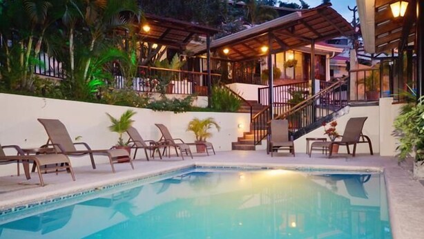 Una piscina con sillones de descanso y un patio cubierto.