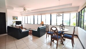 Un salón espacioso con televisión de pantalla plana, ventilador de techo y comedor con mesa y sillas.