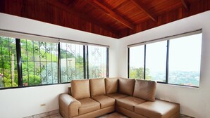 Habitación de esquina con un sofá seccional de cuero marrón, ventanas amplias con barrotes de metal y piso de baldosas.