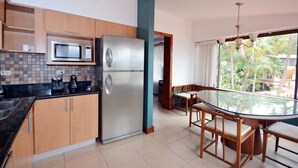 Una cocina moderna con microondas integrado, refrigerador de acero inoxidable y una mesa de comedor de vidrio con sillas de madera.