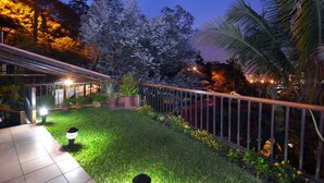 Un espacio exterior bien iluminado con un patio de baldosas, una cerca de metal y diversas plantas en macetas.