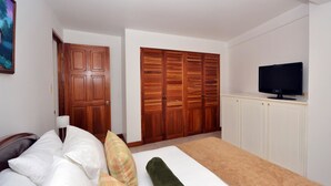 Un dormitorio con cama, almohadas, televisor, armarios de madera y una puerta.