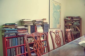 A study room with a large desk, wooden chairs, and bookshelves filled with books.