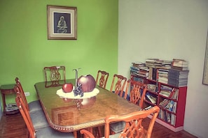 A dining area with a wooden table and chairs, a bookshelf filled with books, and a framed picture on the wall.