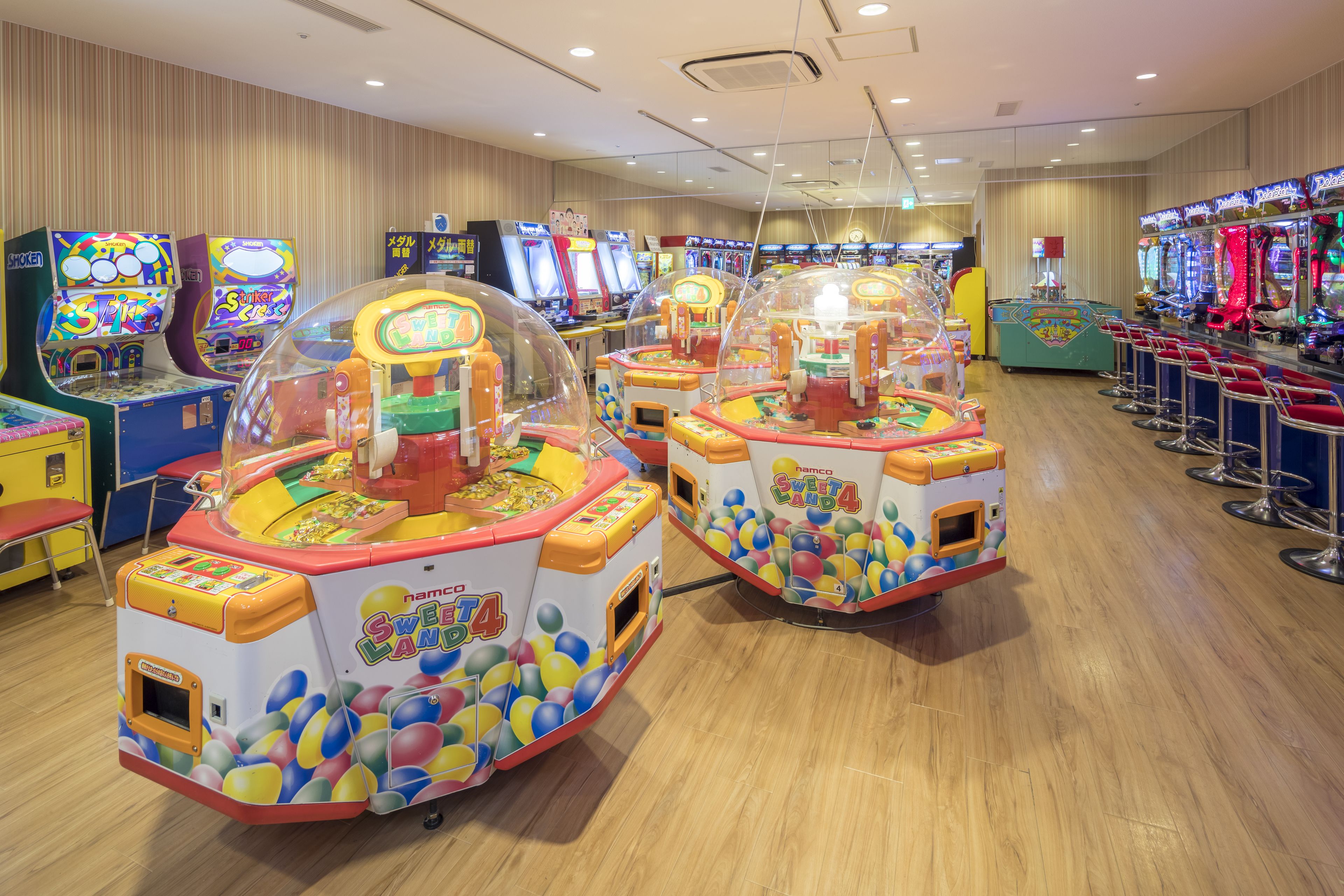 An arcade with multiple gaming machines, including 'Sweet Land' and 'Hank's Arcade' games, and a row of red bar stools.