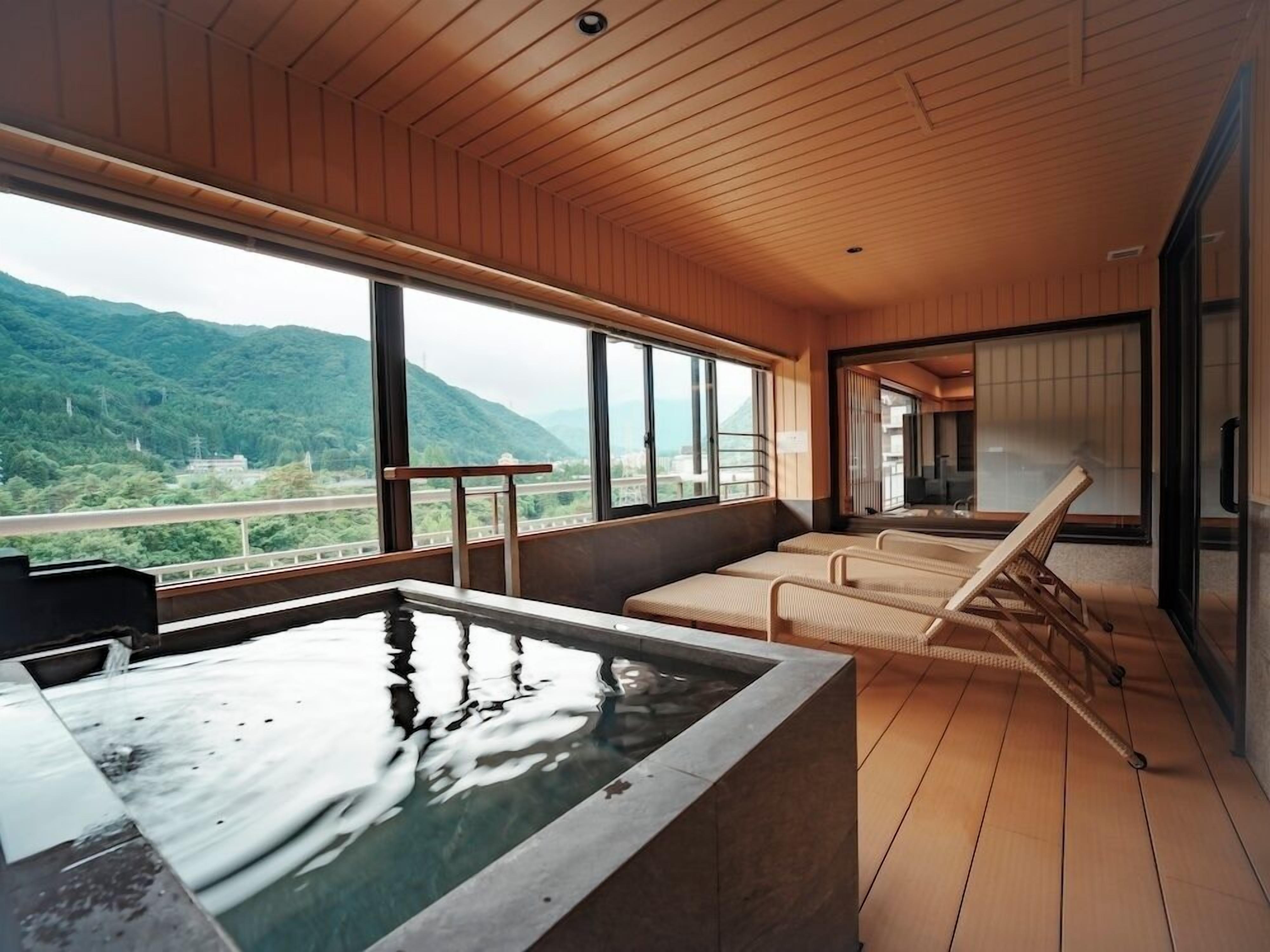 A room with a wooden ceiling, a hot tub, and a view of green mountains.