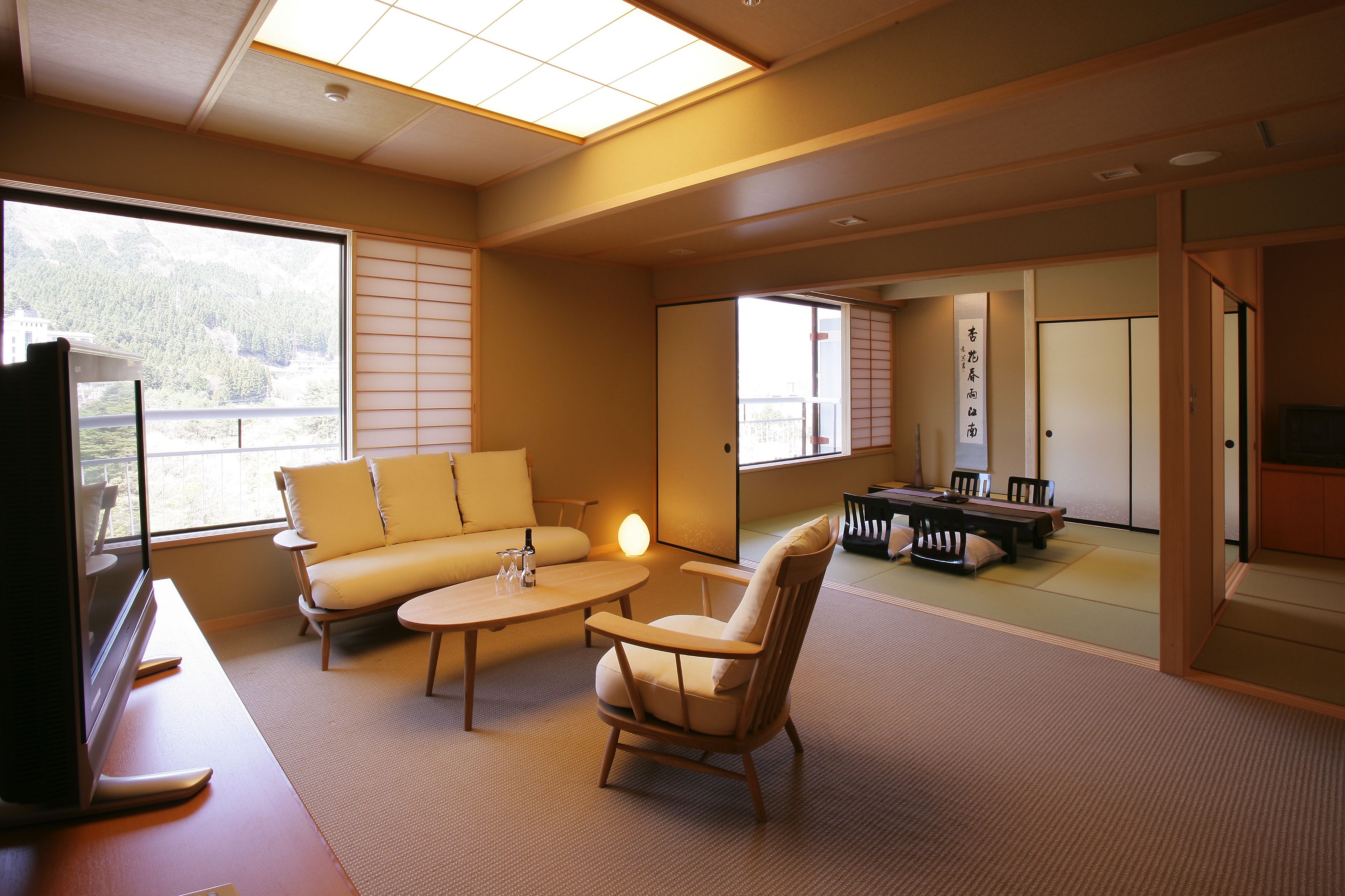 A traditional Japanese room with tatami flooring, a low table with cushions, a sofa, and a television.