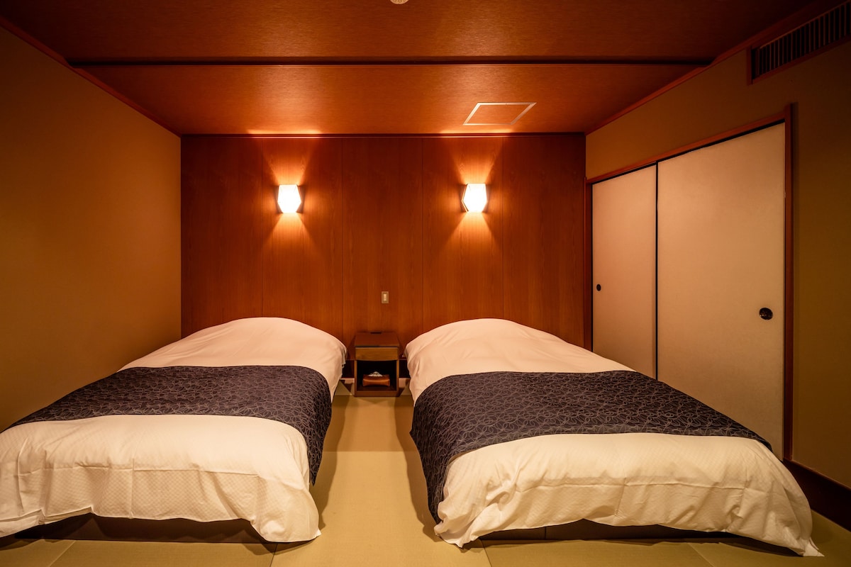 Habitación de hotel con dos camas, paneles de madera en las paredes y una puerta corrediza.
