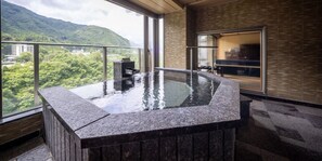 Un bain à remous avec vue sur un paysage montagneux, un banc en bois et une porte vitrée donnant sur une pièce.