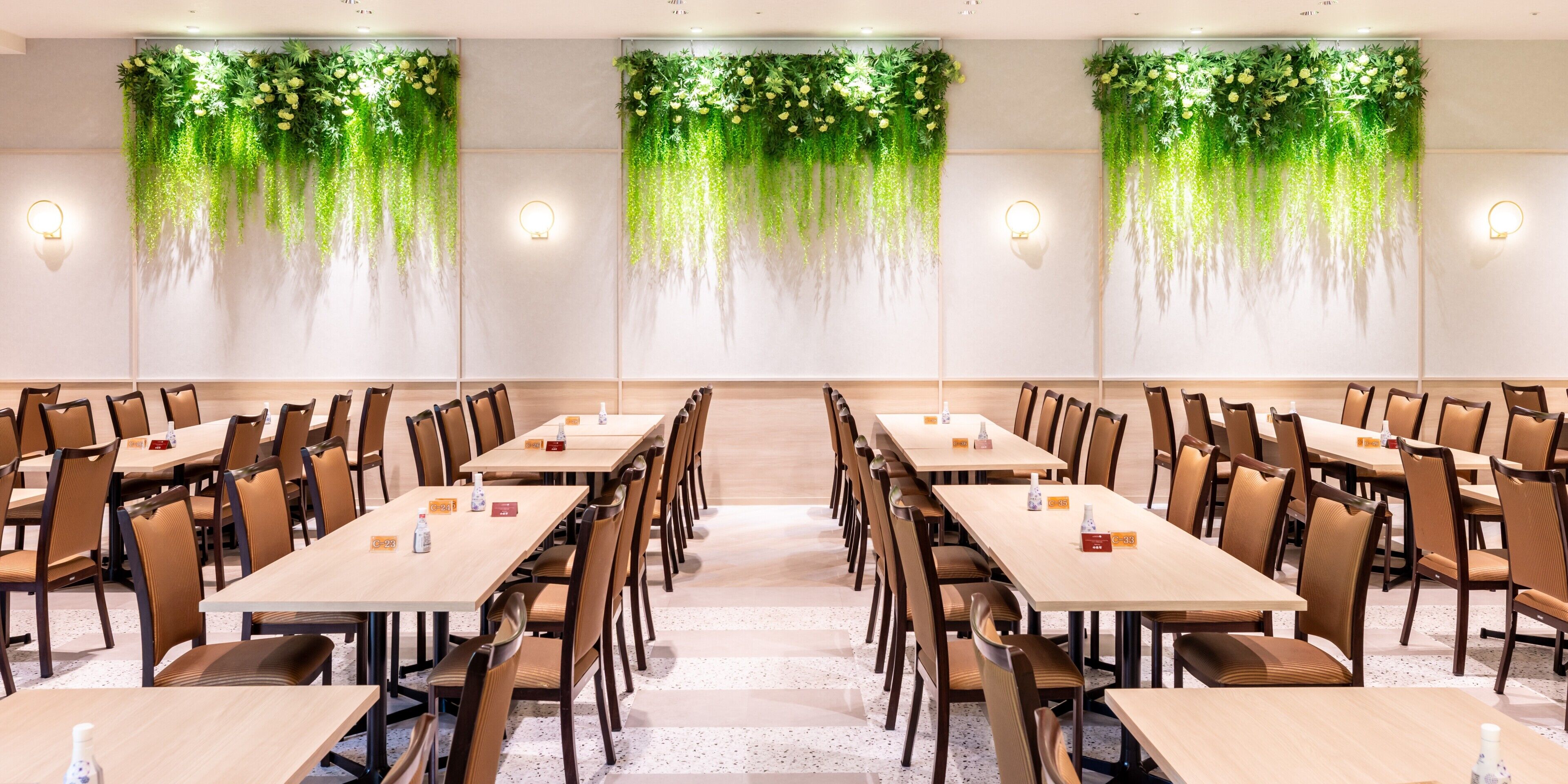 A conference room with long tables and chairs, green hanging plants, and wall sconces.