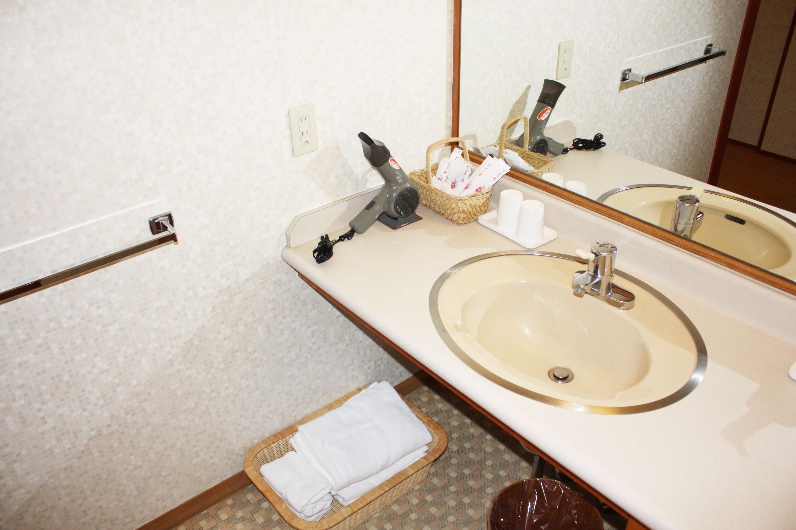 A bathroom with two sinks, a mirror, a hairdryer, a basket with toiletries, and a towel rack.