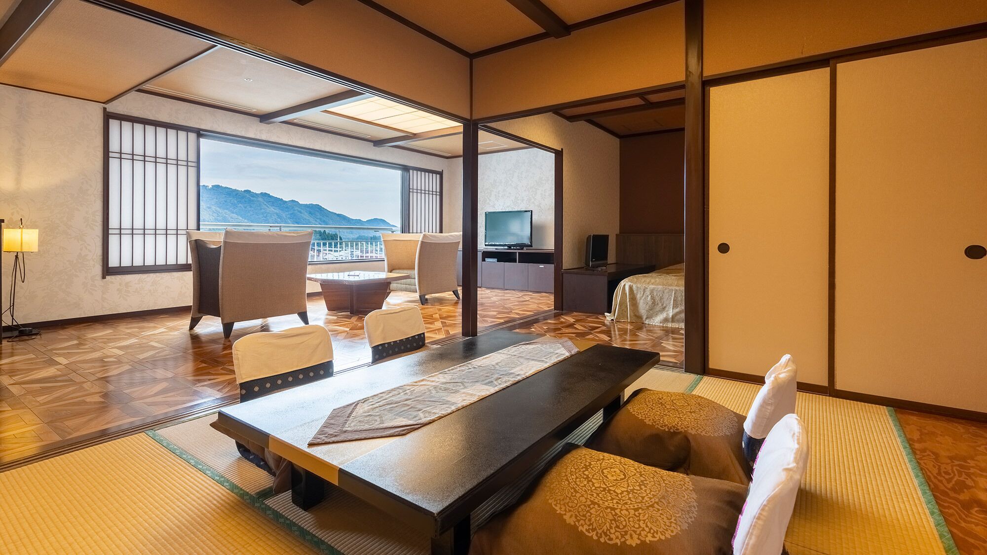 Ein traditioneller japanischer Raum mit Tatami-Böden, einem niedrigen Tisch, Stühlen, einem Bett und einem Fernseher.