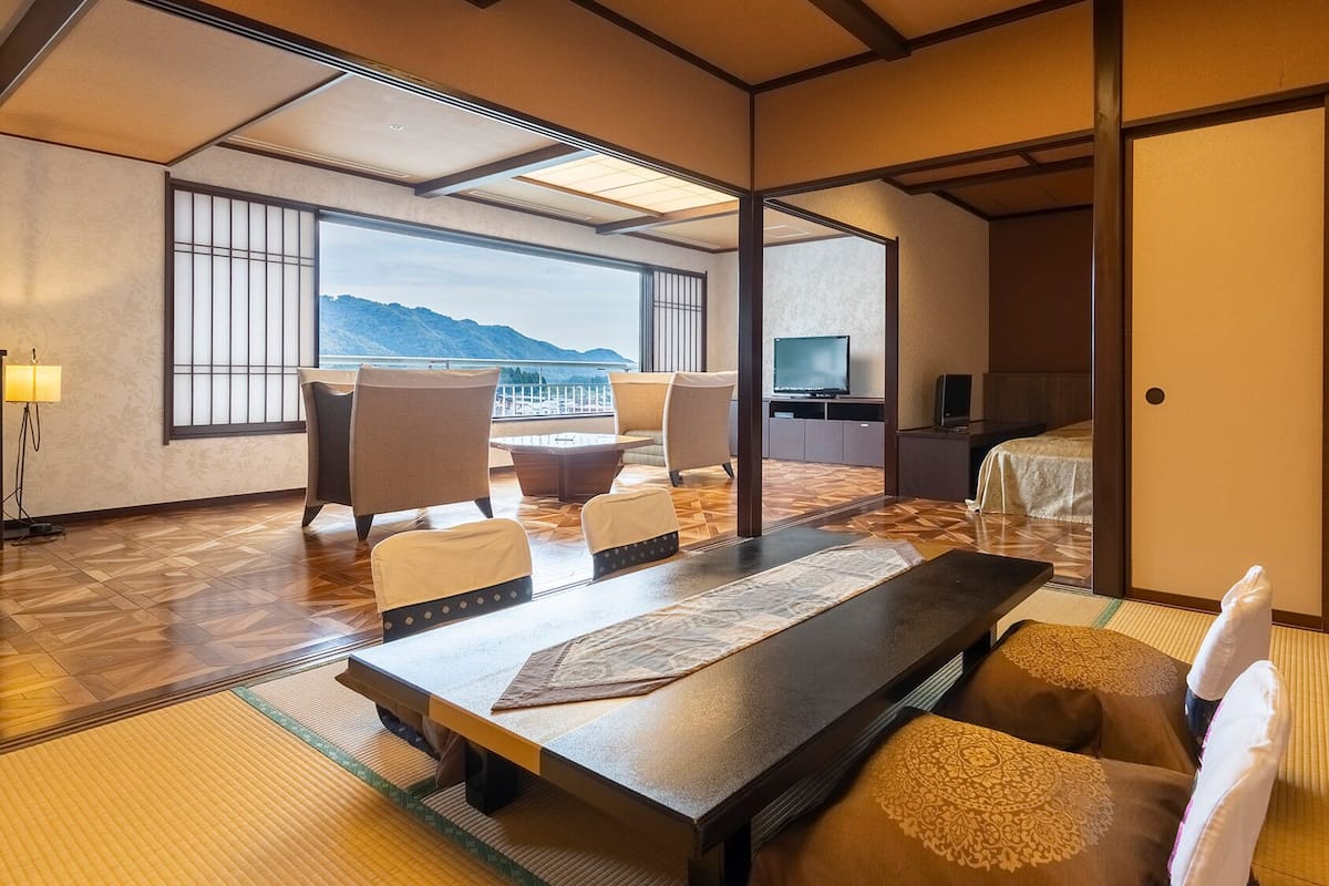 Ein traditioneller japanischer Raum mit Tatami-Böden, einem niedrigen Tisch, Stühlen, einem Bett und einem Fernseher.