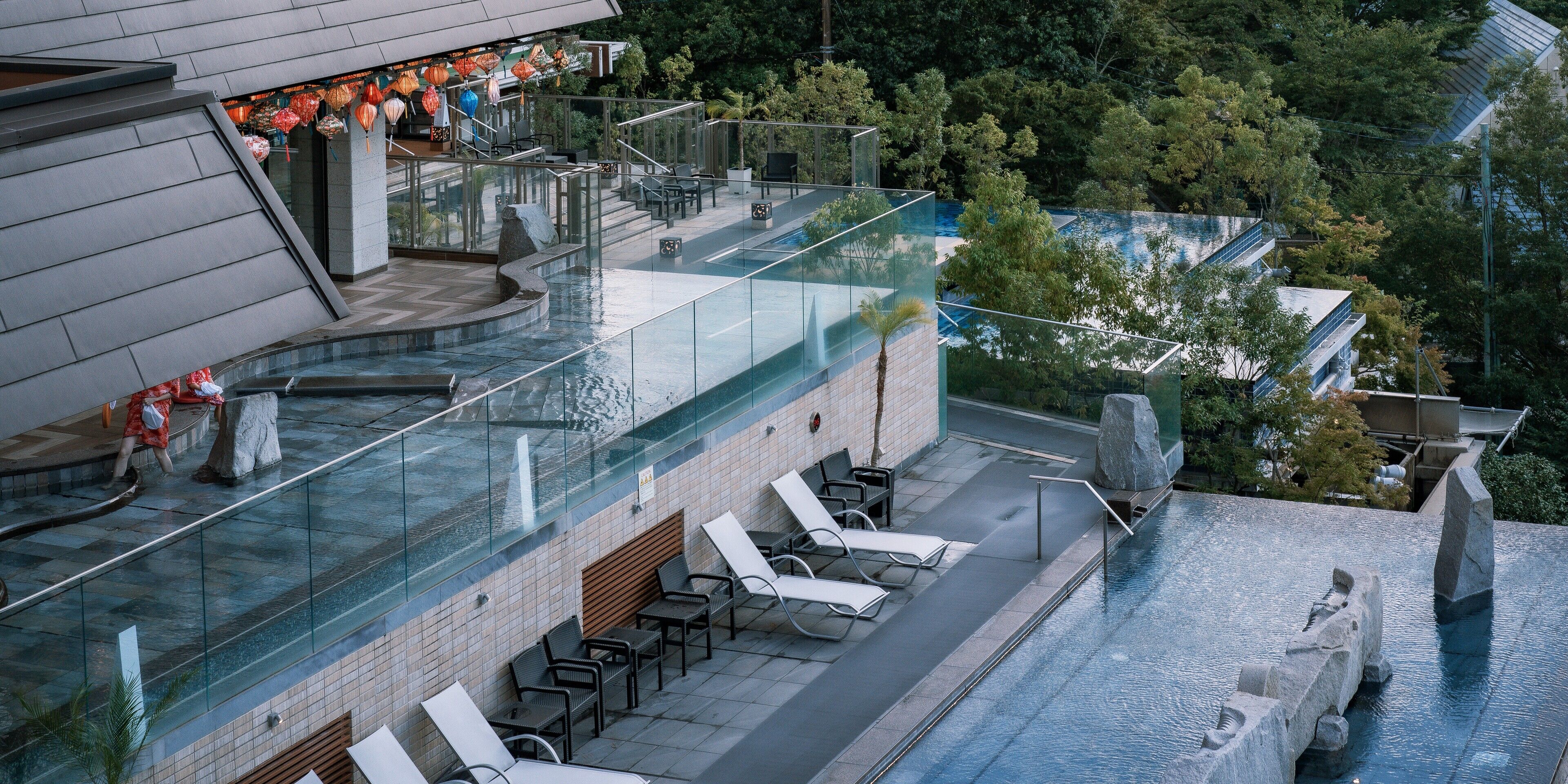 A rooftop pool with glass railings, lounge chairs, and a stone sculpture.