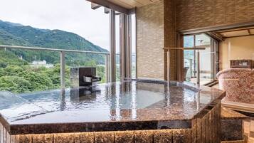 Relax in a serene mountain setting with a panoramic view, featuring a large hot tub and stone bench.