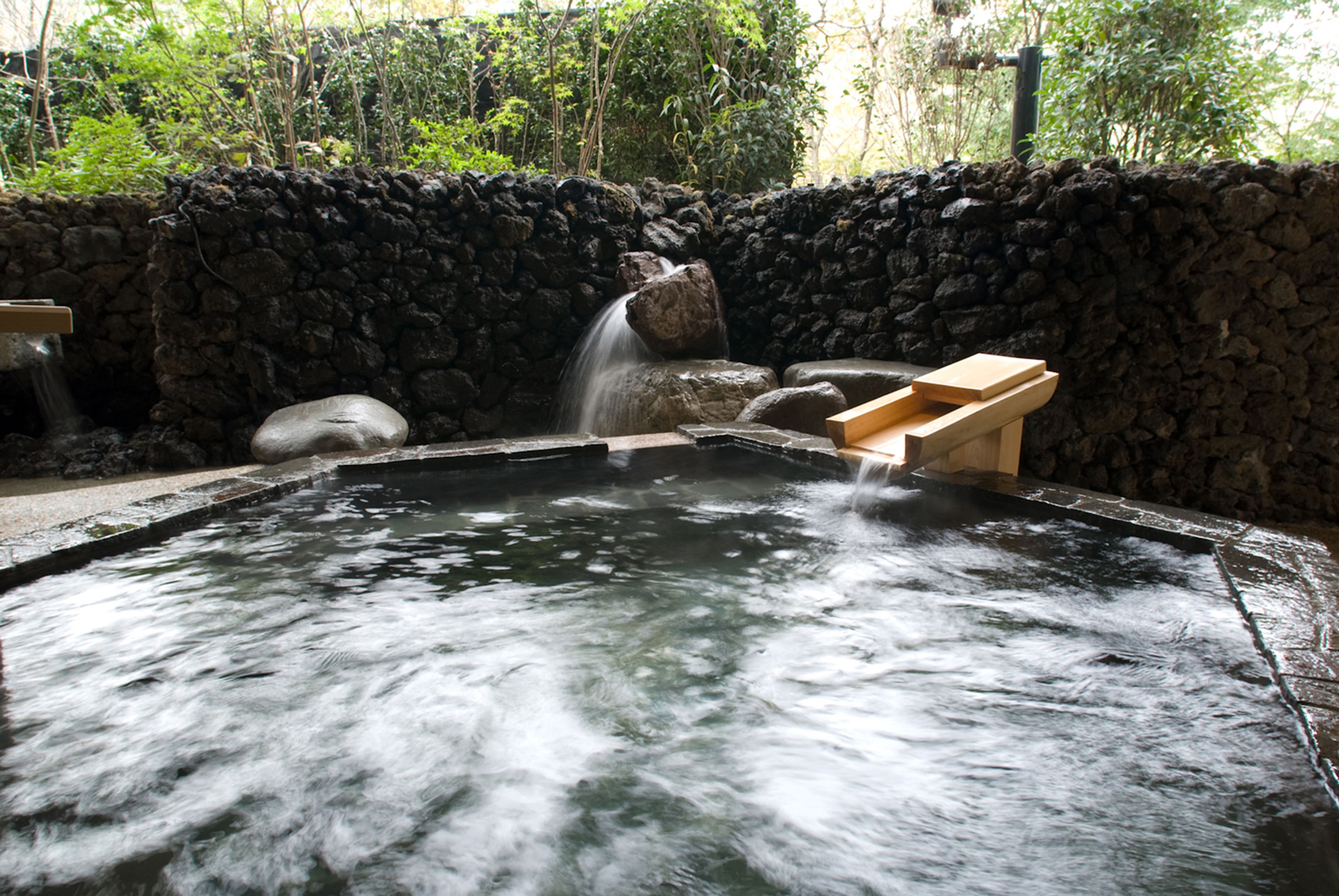 A hot spring with a stone wall and wooden benches.