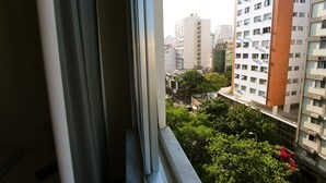 Vista desde una ventana que da a un paisaje urbano con edificios altos, áreas verdes y cielo despejado.