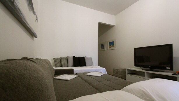 Una habitación de hotel moderna con sofá, cama con ropa de cama blanca, televisor de pantalla plana y una mesita auxiliar.