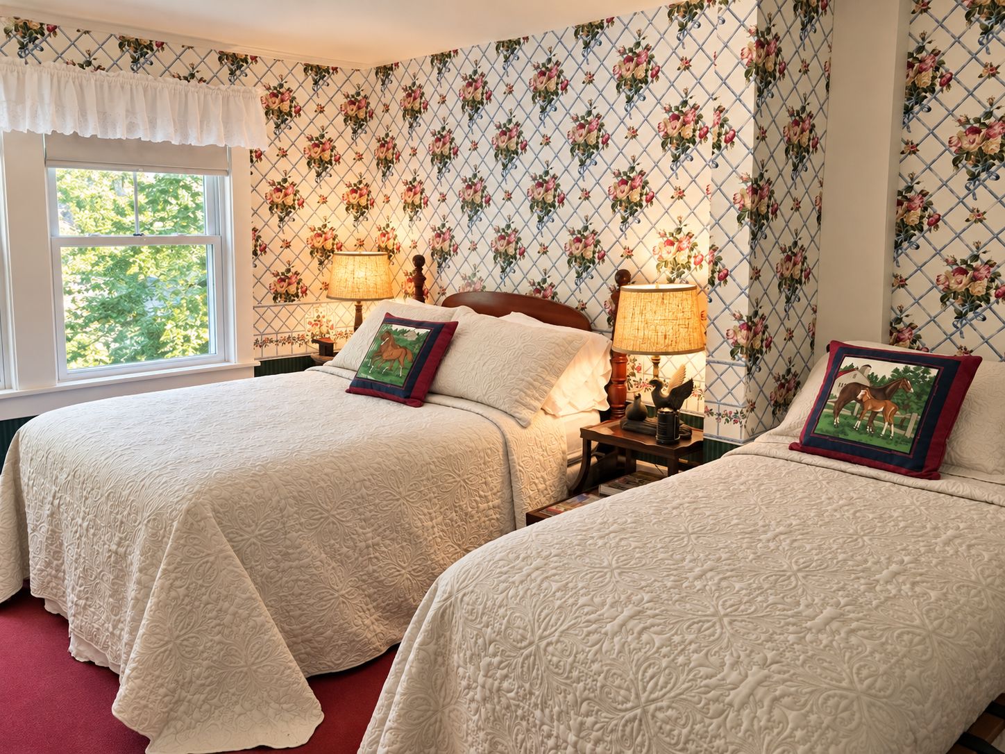 A bedroom with two beds, floral wallpaper, and a window with a view of trees.