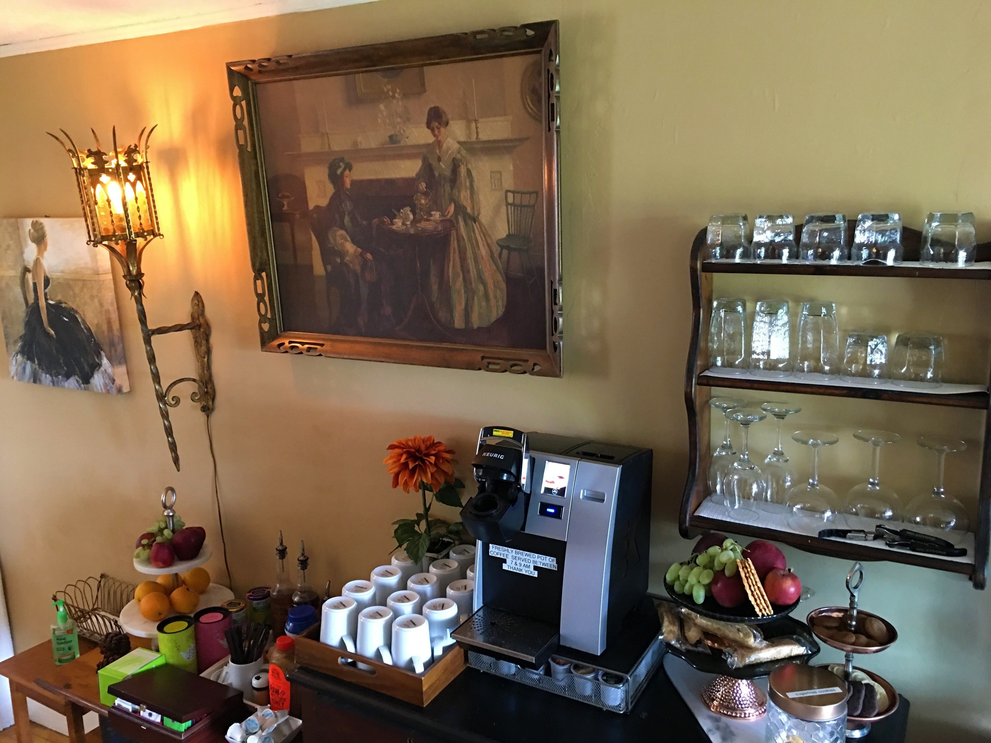 Una estación de café con una máquina Keurig, una exhibición de frutas y un cuadro en la pared.