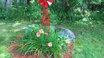 Un jardin avec un moulin à vent rouge, des plantes en fleurs et un grand rocher.
