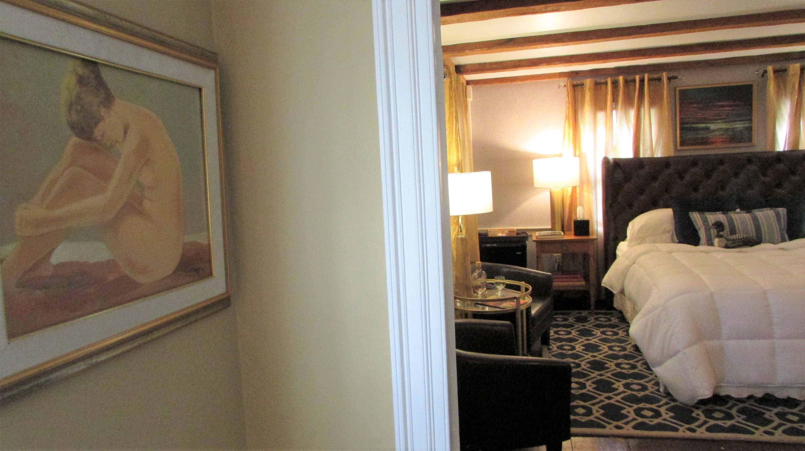 Habitación de hotel con una cama grande, un escritorio con lámpara, una silla y un cuadro en la pared.