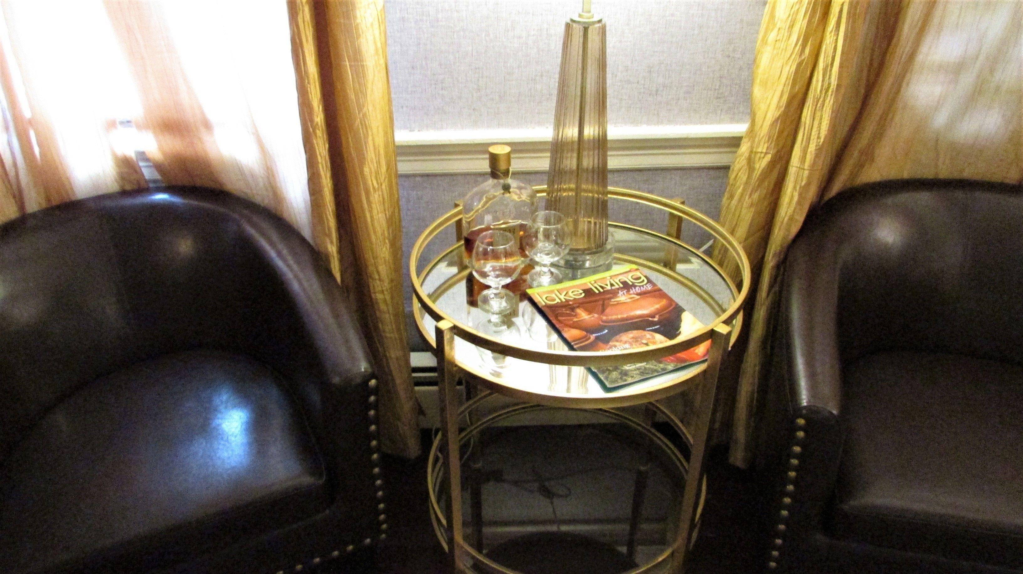 A small table with a magazine, glasses, and a bottle. Two leather chairs are positioned on either side of the table.