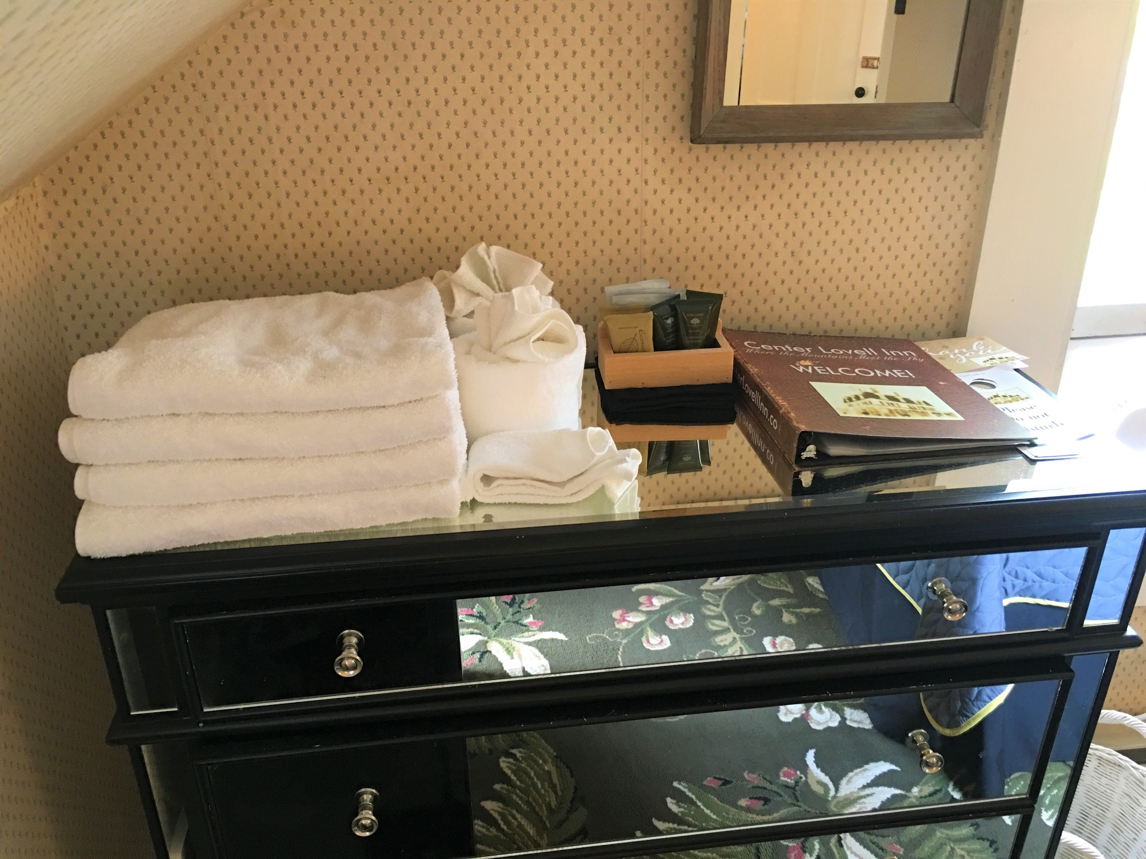 Un mostrador de recepción de hotel con una pila de toallas blancas, un libro de visitas y una pequeña caja de madera.
