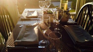 Une table dressée pour un repas, avec une bouteille de vin, des verres et une vue sur une rivière et la verdure environnante.