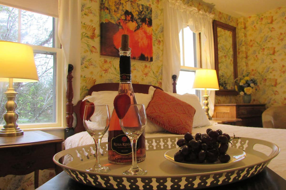 A hotel room with a bed, two bedside lamps, a tray with a bottle of wine, glasses, and a plate of grapes.