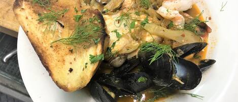 A seafood dish with mussels, clams, shrimp, and a piece of grilled bread, garnished with herbs.
