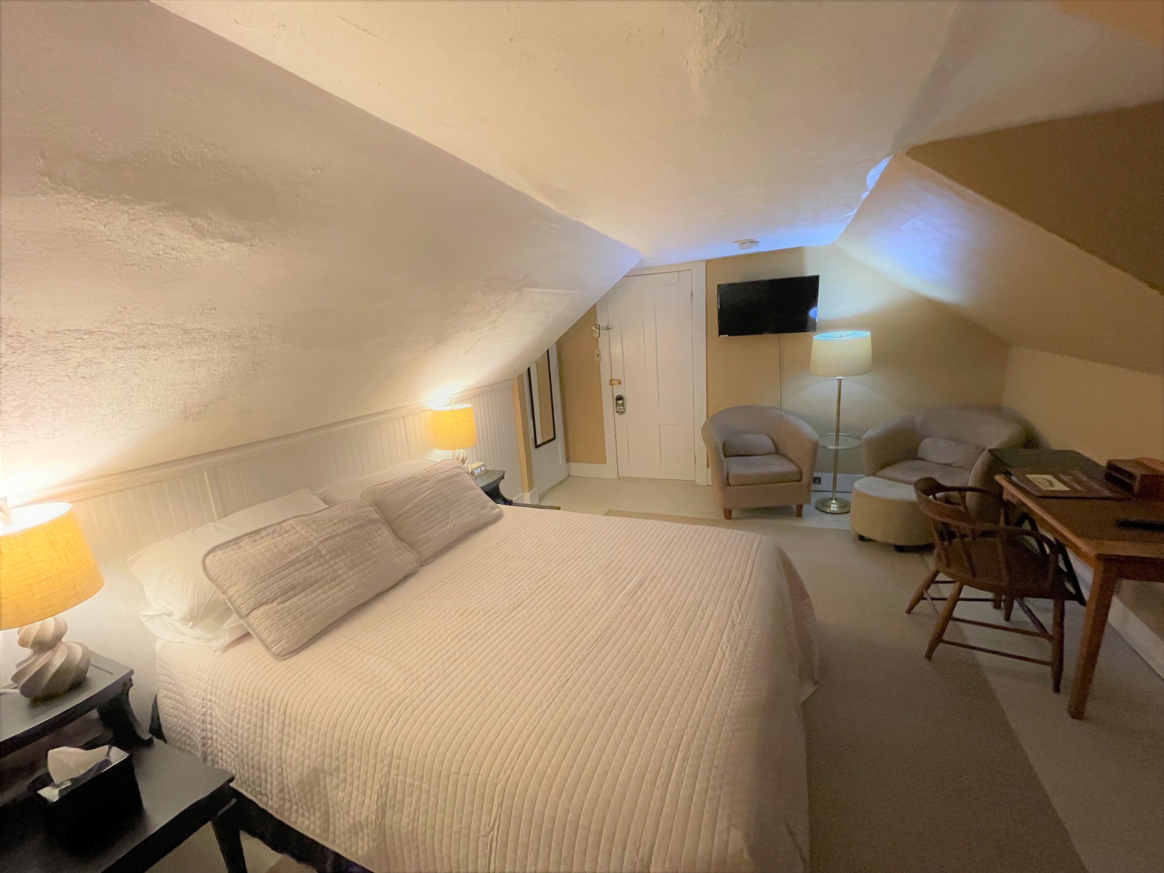 A hotel room with a bed, bedside tables, a desk, a chair, and a TV mounted on the wall.