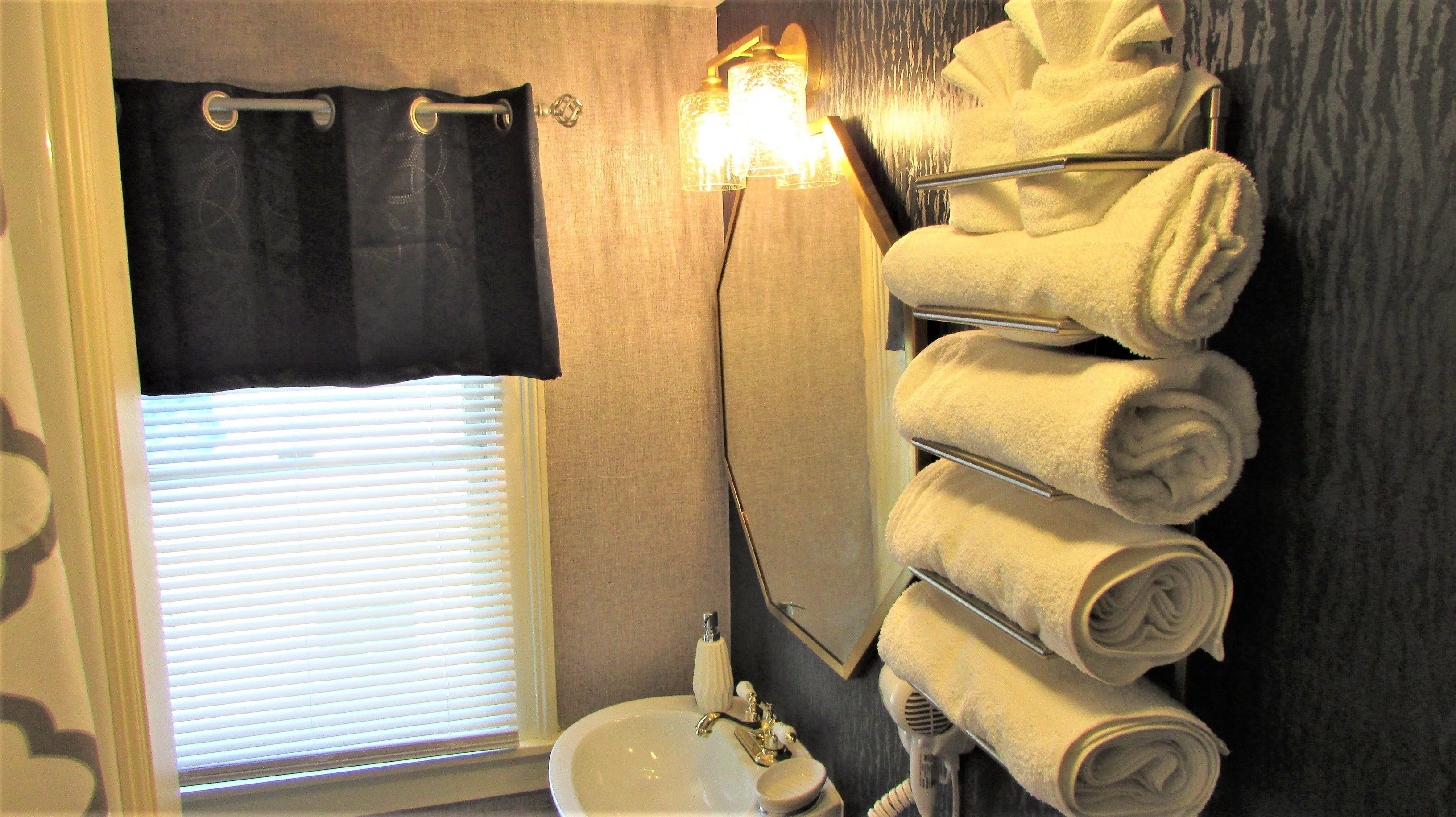Une salle de bain équipée d’un lavabo, d’un miroir, d’un porte-serviettes avec des serviettes et d’une fenêtre avec des stores.