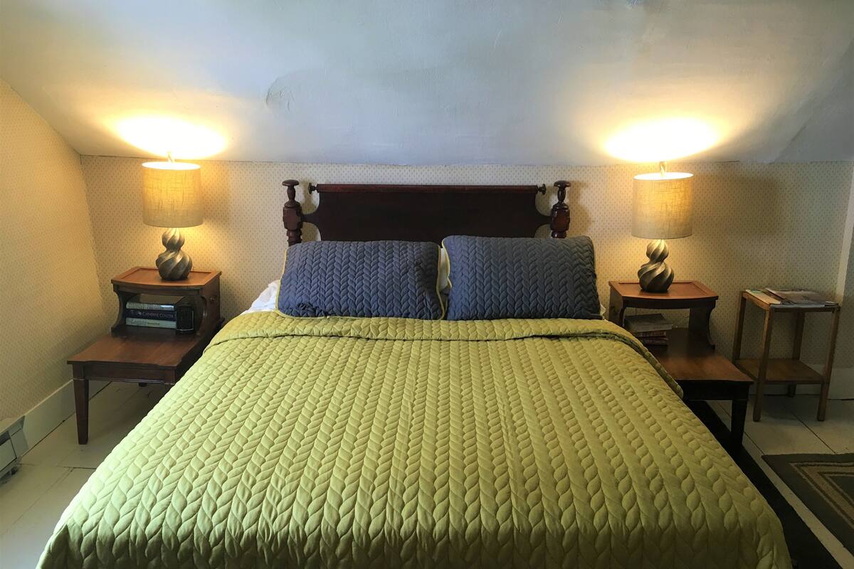 A neatly made bed with a green quilt, two pillows, and two bedside lamps on wooden nightstands.