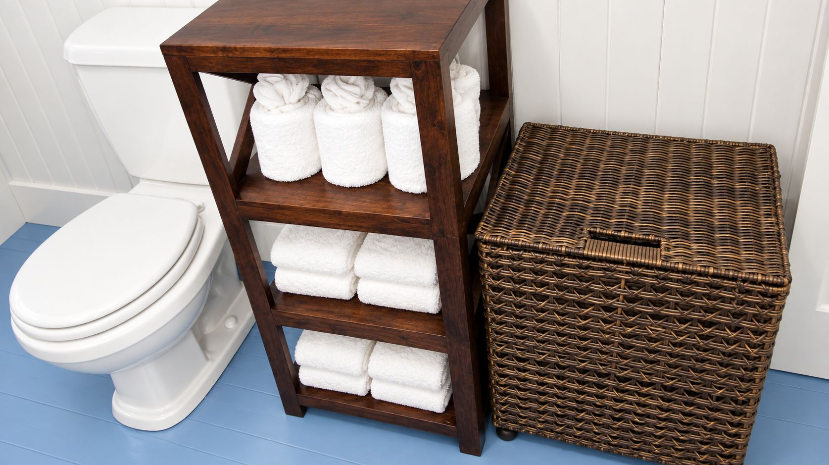 A bathroom with a white toilet, a wooden shelf with folded towels, and a wicker basket.