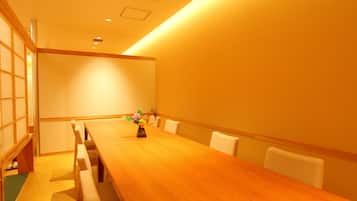 Un salón de conferencias con una larga mesa de madera, sillas blancas y un pequeño jarrón con flores.