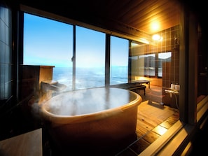 Un baño de vapor con una bañera grande, un banco de madera y vistas al océano a través de amplios ventanales.