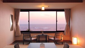 Quarto com vista para o oceano, uma mesa com cadeiras, uma mesinha com um vaso e um abajur.