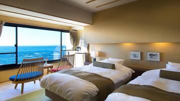 A hotel room with two beds, a desk, a chair, and a large window offering a sea view.