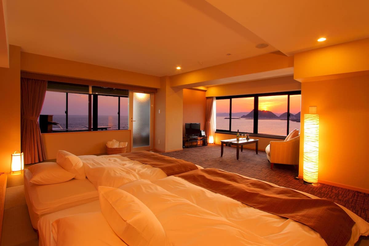 A hotel room with a large bed, a desk, a chair, and a view of the sea.