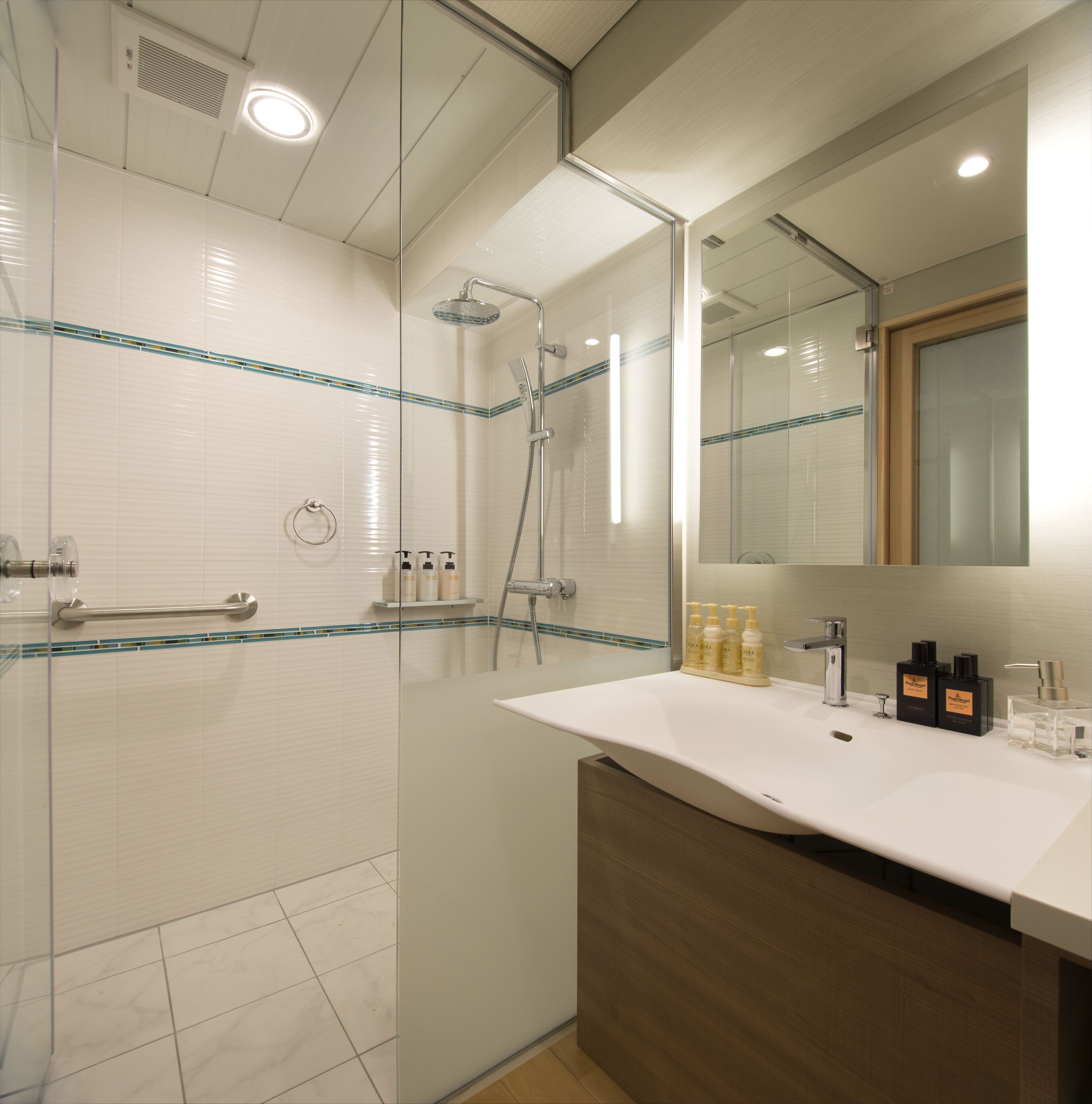 Un baño moderno con cabina de ducha de vidrio, un lavabo blanco con tocador de madera y un espejo grande sobre el lavabo.