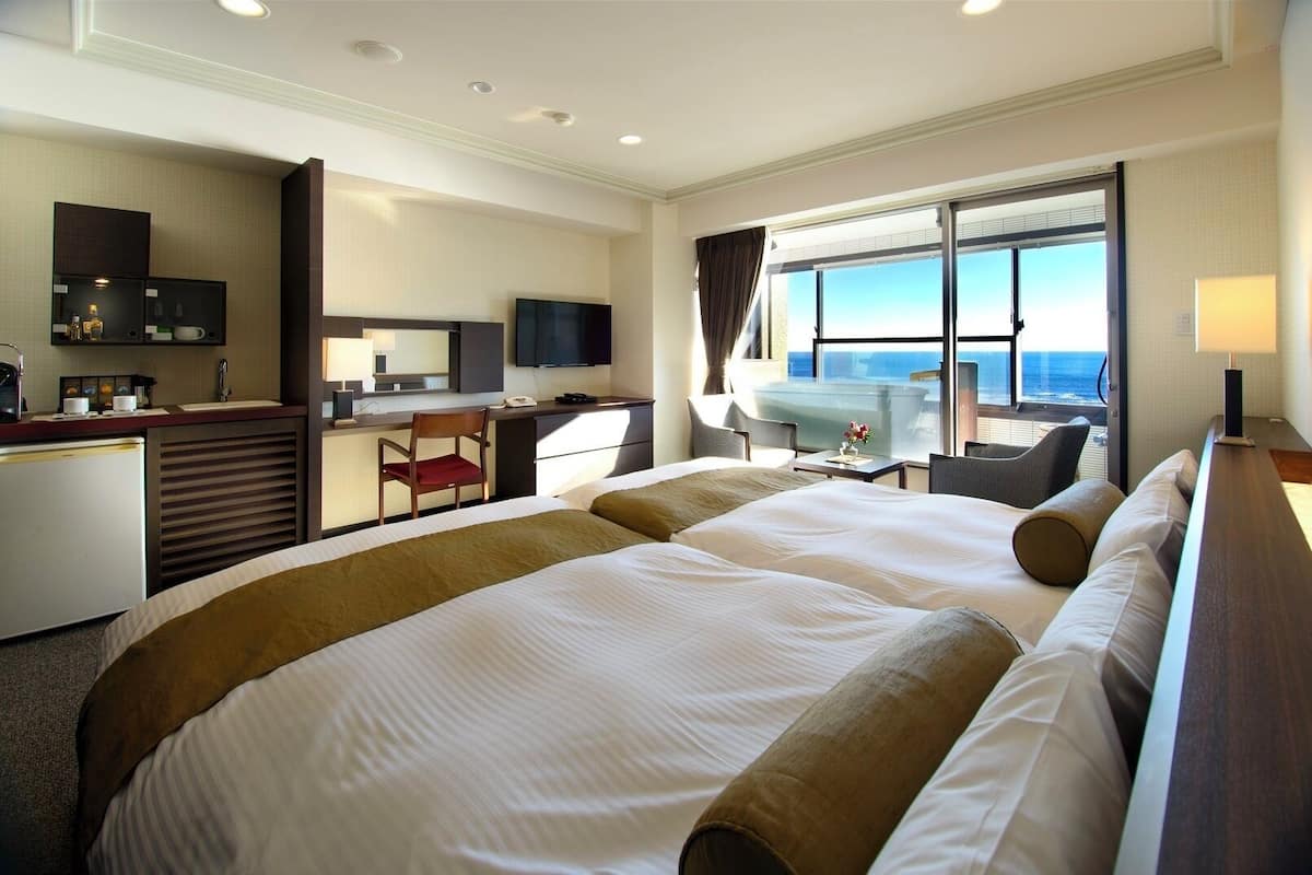 A hotel room with two large beds, a desk with a chair, a television, and a view of the ocean.
