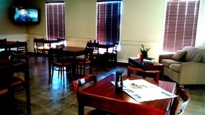 A dining area with wooden tables and chairs, a television mounted on the wall, and a sofa in the corner. - R&R Inn (Provost)