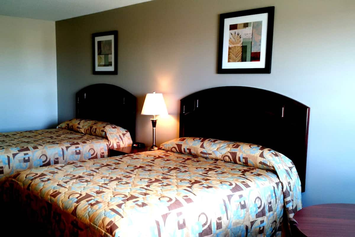 A hotel room with two beds, a bedside table with a lamp, and two framed pictures on the wall.