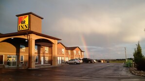 A R&R Inn building with a prominent sign, a parking lot with cars, and a rainbow in the sky. - R&R Inn (Provost)