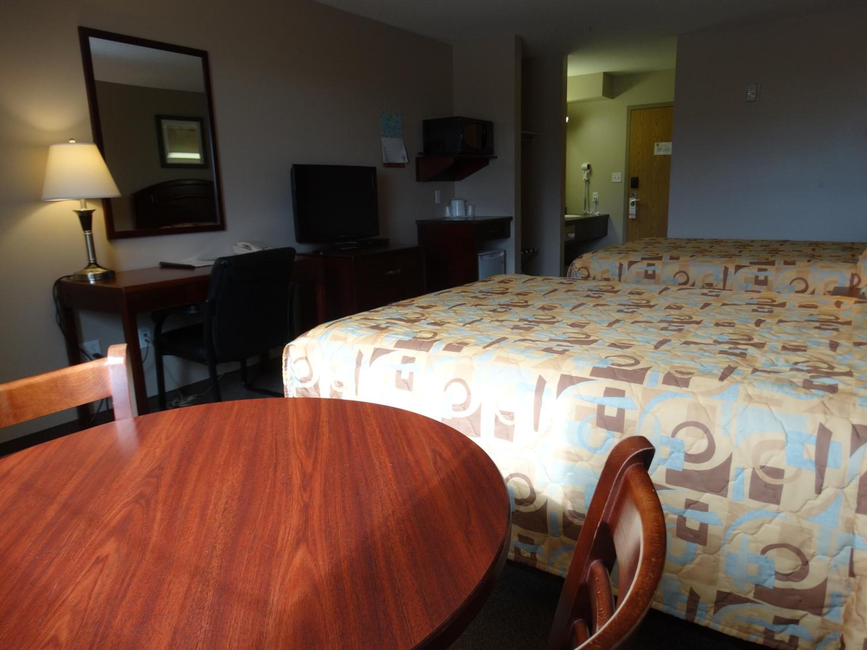 Une chambre d’hôtel avec un bureau en bois, une chaise, un lit avec une literie à motifs, une télévision et un miroir au mur.