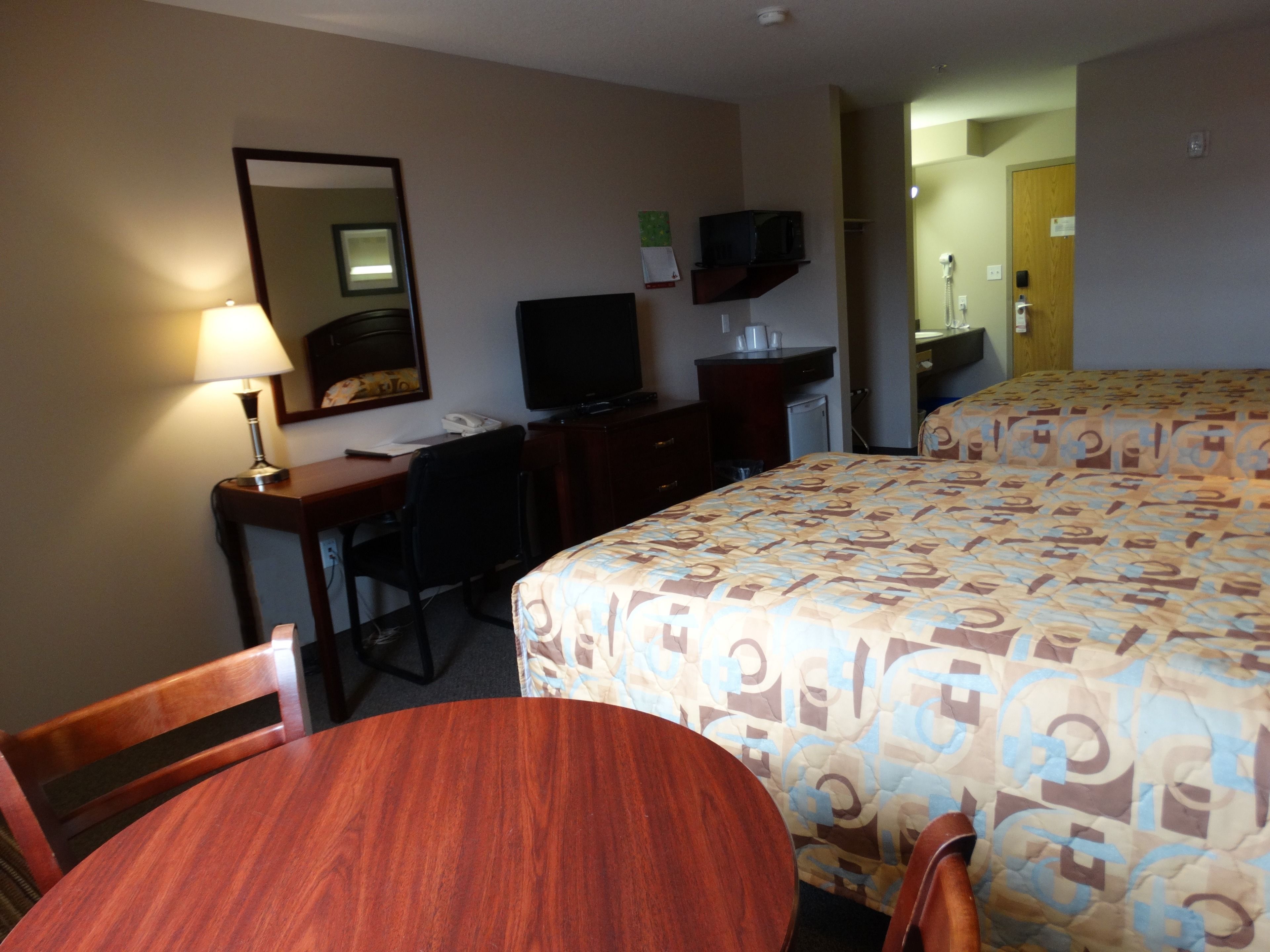 A hotel room with a desk, chair, bed, and a television.